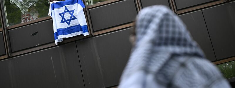 Eine Frau hält eine Israelflagge aus dem Fenster: Die propalästinensische Demonstration auf dem Theaterhof der Freien Universität Berlin wird von Polizisten beobachtet. - Foto: Sebastian Christoph Gollnow/dpa