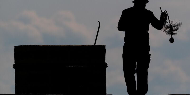 Ein Schornsteinfeger mit seinem Kaminkehrerwerkzeug auf einem Dach. - Foto: Robert Michael/dpa