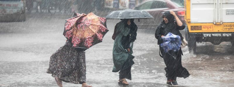 Frauen gehen bei Regen über eine Straße in Bangladesch. - Foto: Md. Rakibul Hasan/ZUMA Press Wire/dpa