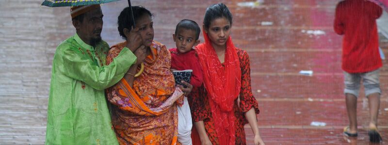 Fußgängerinnen gehen in Bangladesh durch den Regen. - Foto: Md Rafayat Haque Khan/ZUMA Press Wire/dpa