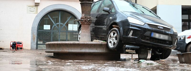 Auf einem Brunnen in Rudersberg hängt ein durch das Hochwasser weggespültes Auto. - Foto: dpa