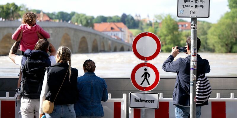 Menschen schauen sich in der Altstadt am Donauufer hinter einer Schutzwand das Hochwasser an. - Foto: Sven Hoppe/dpa