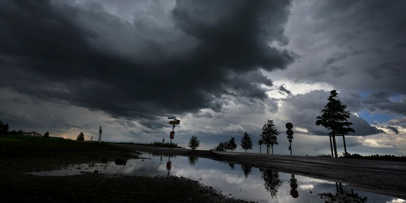 Dichte Regenwolken spiegeln sich in einer Pfütze. - Foto: Karl-Josef Hildenbrand/dpa
