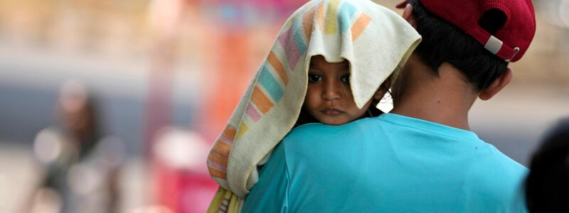 Ein Mann trägt ein Kind, dessen Kopf mit einem Handtuch bedeckt ist. - Foto: Channi Anand/AP/dpa