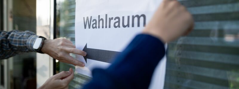 Wahlhelfer hängen einen Zettel, auf dem „Wahlraum“ steht, auf. - Foto: Fabian Strauch/dpa