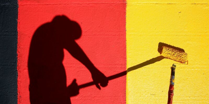 Heute Abend geht es los! Ein Helfer lackiert Kurvensteine in den Farben Schwarz-Rot-Gold. - Foto: Jan Woitas/dpa