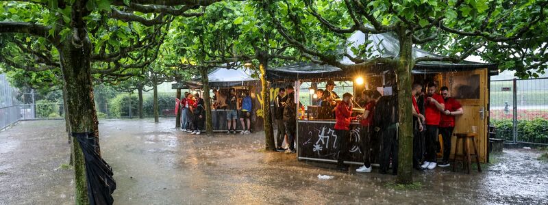 Zumindest ein bisschen Schutz: Fussballfans in Dortmund haben sich beim strömenden Regen an Imbissbuden untergestellt. - Foto: Christoph Reichwein/dpa