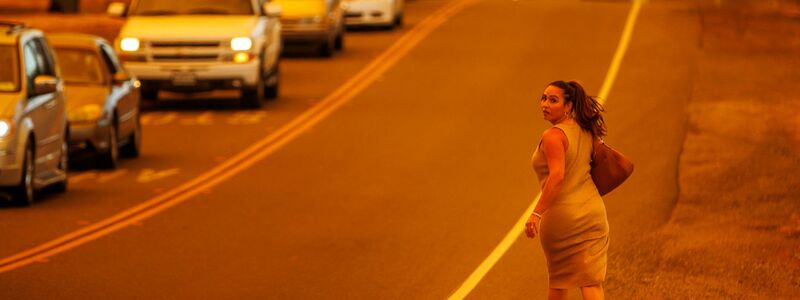 Eine Frau läuft an einer Straße während das Thompson-Feuer brennt - Foto: Ethan Swope/AP/dpa