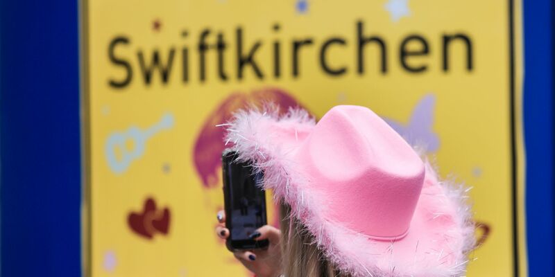 Ein Fan fotografiert vor dem Konzert der Sängerin Taylor Swift in Gelsenkirchen ein «Swiftkirchen»-Schild. Während des Konzerts am Abend zog der Datenverbrauch in den Handynetzen in der Veltins Arena kräftig an. - Foto: Oliver Berg/dpa