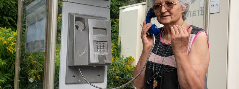 Marie-Claude König nimmt in Murbach einen Anruf entgegen. In der Telefonzelle im Elsass rufen Menschen aus der ganzen Welt an. - Foto: Florian Bodenmüller/SWD - Südwestdeutsches Mediennetzwerk GmbH/dpa