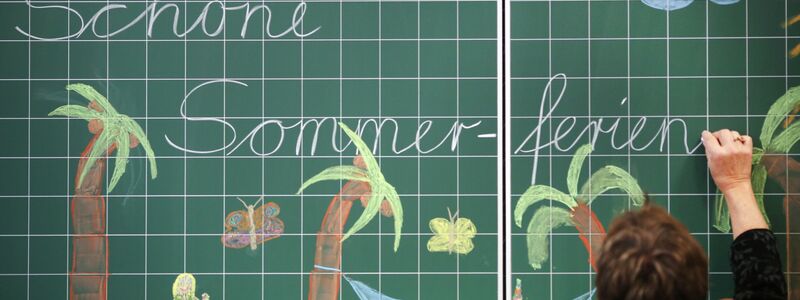 Eine Lehrerin schreibt «Schöne Sommerferien» an die Tafel einer Grundschulklasse. (Archivfoto) - Foto: Ina Fassbender/dpa