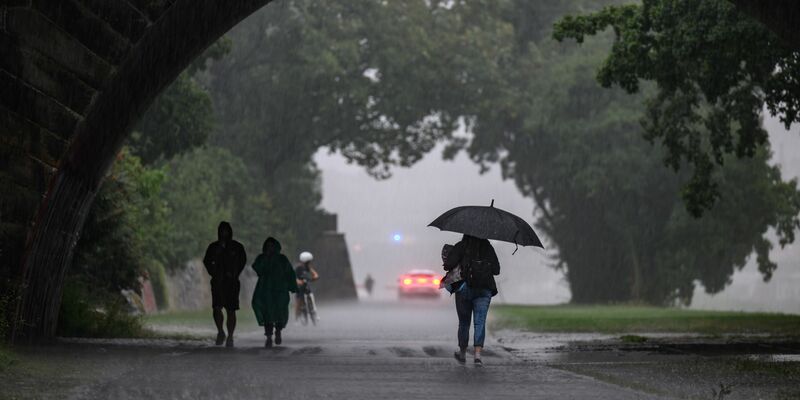 Menschen sind bei starkem Regen in Dresden während eines Gewitters auf dem Elberadweg unterwegs. - Foto: Robert Michael/dpa