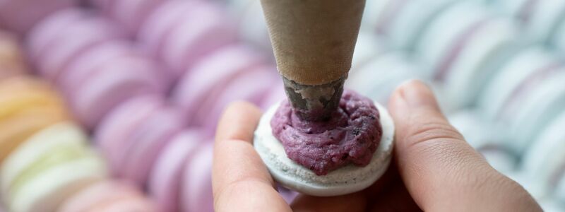 Das Baisergebäck Macaron wird in einer Bäckerei mit einer Spritztüte befüllt. (Archivbild) - Foto: Sebastian Kahnert/dpa