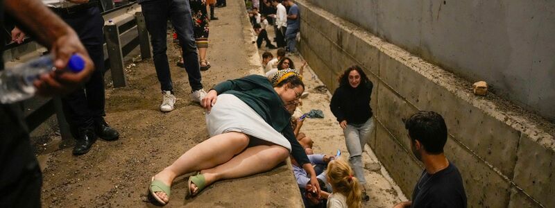 Menschen gehen am Straßenrand in Deckung, während eine Sirene auf einer Autobahn vor ankommenden Raketen warnt. - Foto: Ohad Zwigenberg/AP/dpa