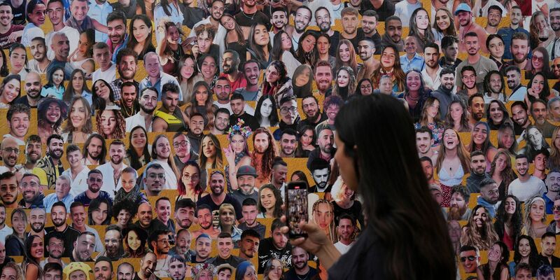 Eine Frau fotografiert eine Wand mit Porträts der Opfer am Ort des Nova-Musikfestivals. (Archivbild) - Foto: Ariel Schalit/AP/dpa