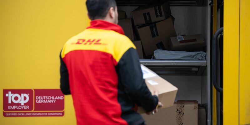 Ein Post-Mitarbeiter trägt ein Paket in einen Lieferwagen. - Foto: Hannes P. Albert/dpa