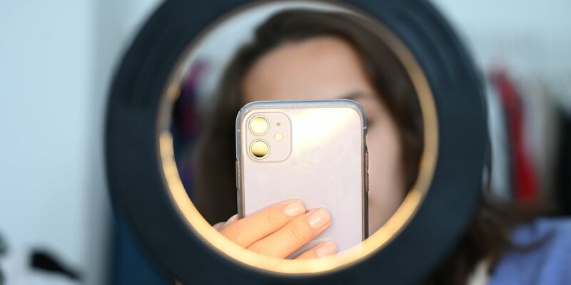 Eine Frau sitzt hinter einem Ringlicht und macht dabei Aufnahmen von sich (Symbolbild) - Foto: Niklas Graeber/dpa