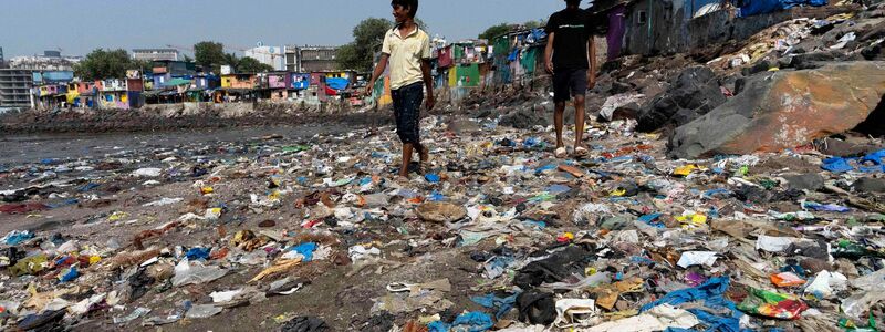 Menschen spazieren am Strand des Badhwar Park im indischen Mumbai an Plastikmüll vorbei. (Archivbild) - Foto: Rajanish Kakade/AP/dpa