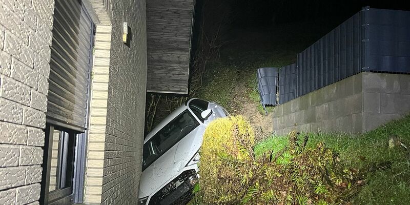 Das Auto steckt zwischen einem Abhang und dem verklinkerten Wohnhaus fest. - Foto: -/Kreispolizei Paderborn/dpa