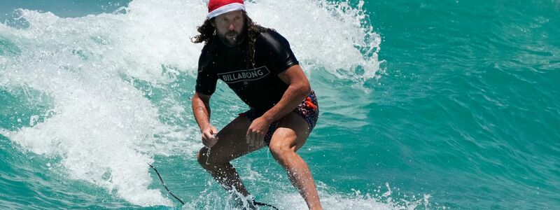 Surfende Santas gehören in Australien zu Weihnachten dazu. (Archivbild) - Foto: Rick Rycroft/AP/dpa