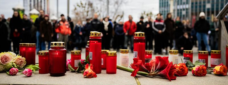 Menschen zünden Kerzen an und legen Blumen nieder. - Foto: Christoph Soeder/dpa