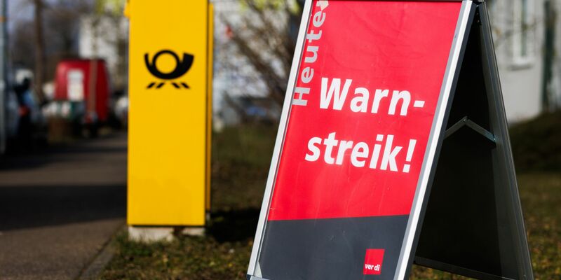 Ein Warnstreik-Schild bei einem Post-Standort, daneben ein Briefkasten - im Ringen um einen Tarifabschluss haben Tausende Postler erneut die Arbeit niedergelegt. - Foto: Philipp von Ditfurth/dpa