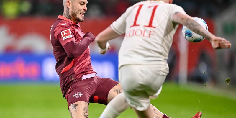 Augsburgs Torwart Finn Dahmen kauert bedröppelt am Boden, die Leipziger Assan Quedraogo (M) und Christoph Baumgartner (r) bejubeln das 0:5.  - Foto: Harry Langer/dpa