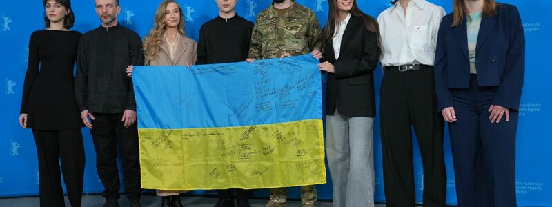 Das Team des Films «Strichka chasu» mit einer ukrainischen Flagge, auf der die Lehrerkollegen des Protagonisten und jetzigen Soldaten Borys Khovriak (M) unterschrieben haben.  - Foto: Soeren Stache/dpa