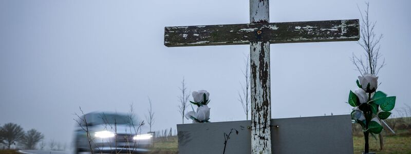 in Auto fährt auf einer Landstraße an einem hölzernen Kreuz vorbei, welches zur Erinnerung an ein Unfallopfer aufgestellt wurde. - Foto: Jens Büttner/dpa