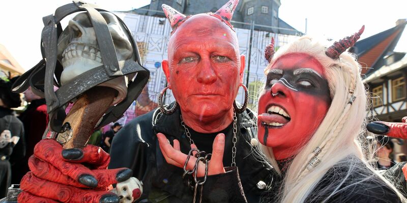 Im Teufelskostüm stehen Besucher auf dem Marktplatz in Wernigerode. - Foto: Matthias Bein/dpa