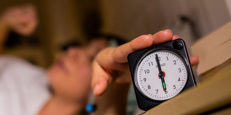 Eine Frau schaltet vom Bett aus einen auf sechs Uhr gestellten Wecker aus. - Foto: Christoph Soeder/dpa