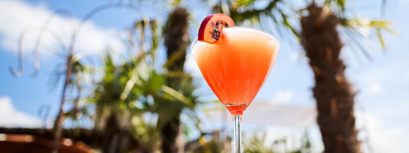 Ein Passionsfrucht Martini (auch Pornstar Martini oder Maverick Martini genannt) steht unter Palmen auf einem Tisch in einer Strandbar. - Foto: Christian Charisius/dpa