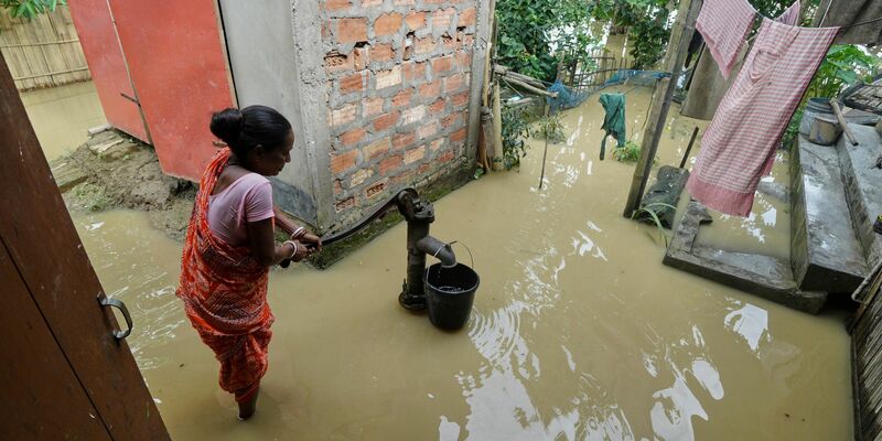 Eine Frau versucht in der überfluteten Umgebung ihres Hauses, Wasser zu sammeln.  - Foto: Uncredited/AP/dpa