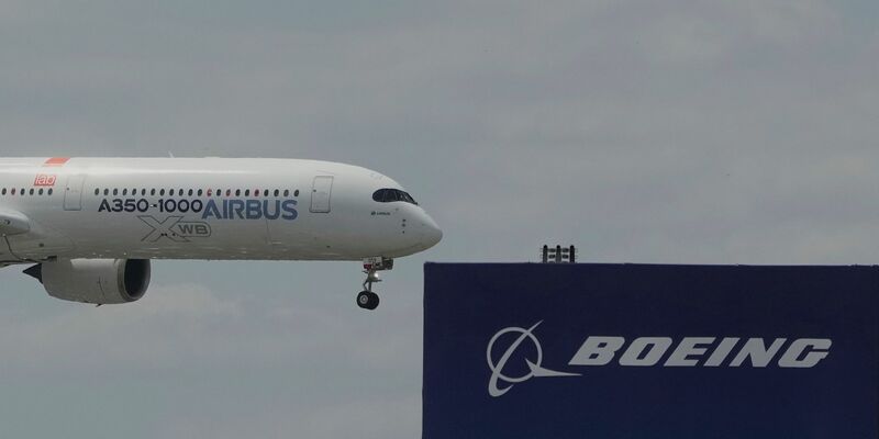 Die zwei großen Konkurrenten: Ein Airbus fliegt bei einer Vorführung auf der Luftfahrtmesse Salon du Bourget an einem Logo von Boeing vorbei. - Foto: Michel Euler/AP/dpa
