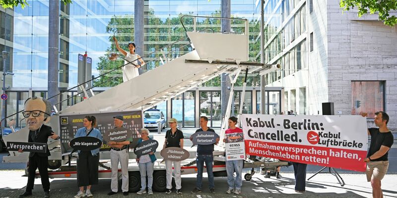 Aktivsten stehen während einer symbolischen Protestaktion am Weltflüchtlingstag zur Unterstützung mehrerer Klagen von Afghanen gegen die Bundesregierung vor dem Auswärtigen Amt. - Foto: Michael Brandt/dpa