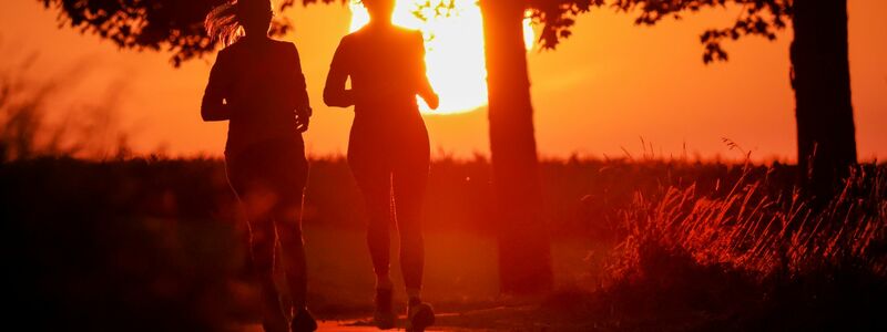 Zwei Frauen joggen am Morgen, während hinter ihnen die Sonne aufgeht. - Foto: Thomas Warnack/dpa