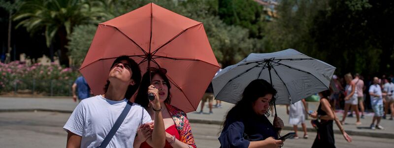 Touristen schützen sich amvor der Kirche Sagrada Familia mit Regenschirmen vor der Sonne.  - Foto: Emilio Morenatti/AP/dpa