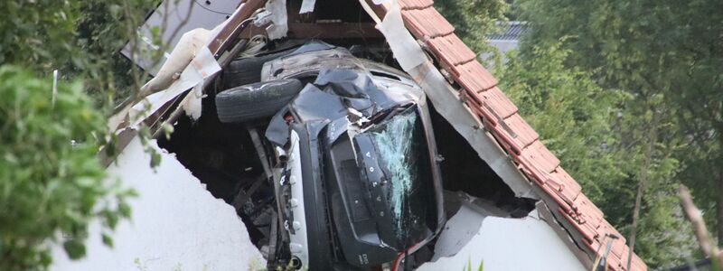 Das Auto liegt nach einem kurzen Flug seitlich in der Mauer einer Scheune. - Foto: -/Moonshine Media/dpa
