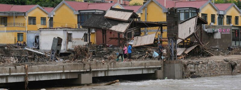 Dorfbewohner versammeln sich in der Nähe einer Brücke, die nach schweren Regenfällen im Bezirk Miyun am Stadtrand von Peking überflutet wurde. - Foto: Andy Wong/AP/dpa