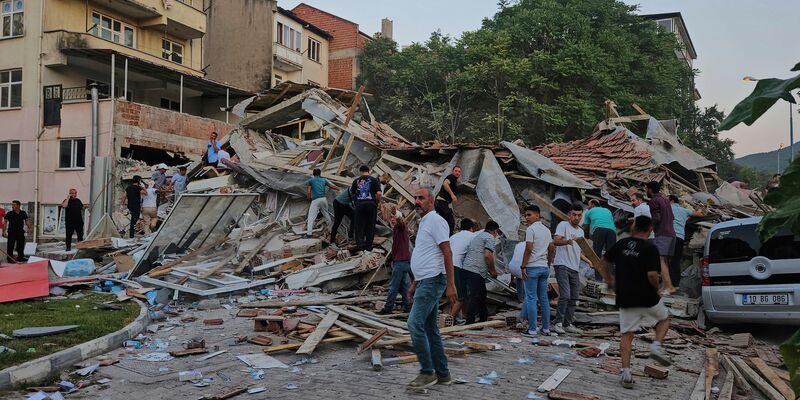 Menschen beseitigen in Sindirgi die Trümmer eines eingestürzten Gebäudes. - Foto: Bahadir Demirceviren/IHA/AP/dpa