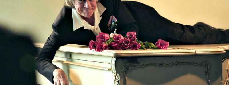 Helge Schneider liegt auf einem Klavier in einer Szene des Films «Helge Schneider - The Klimperclown», der nun in der Mediathek zu sehen ist und am Mittwoch, 20.8., im Ersten gezeigt wird. - Foto: -/SWR Presse/Bildkommunikation/dpa