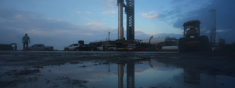 Mehrere Fahnen, darunter zwei mit dem Aufdruck SpaceX und Elon Musk, sind in der Nähe des Startortes. - Foto: Eric Gay/AP/dpa