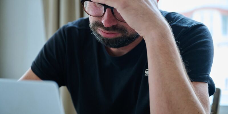 Eine Frau sitzt vor einem geschlossenen Laptop und seufzt. - Foto: Annette Riedl/dpa