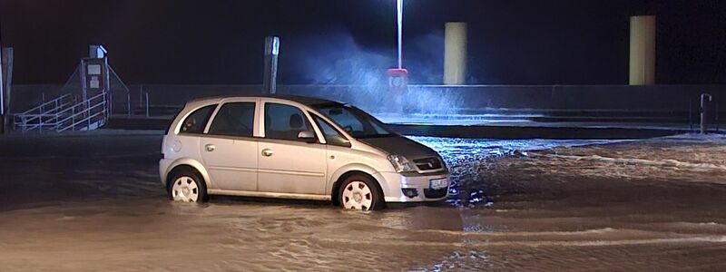 In Wilhelmshaven steht ein Auto auf einem überfluteten Parkplatz.  - Foto: Kai Moorschlatt/dpa