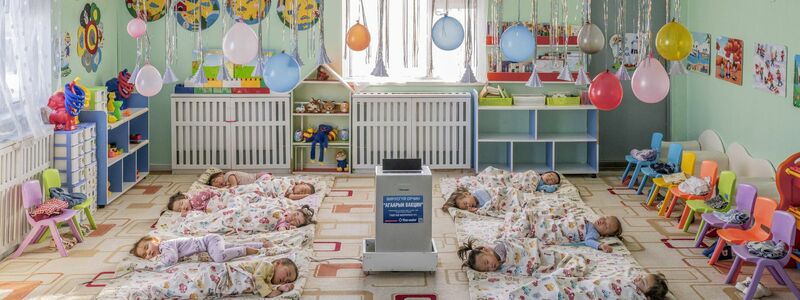 In einem Kindergarten in Ulaanbaatar, der Hauptstadt der Mongolei, liegen Kinder auf dem Boden um einen aufgestellten Luftfilter herum, der die Schadstoffkonzentration senken soll. - Foto: Natalya Saprunova/Unicef/dpa