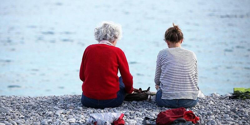 Alte und junge Frau sitzen am Strand - Foto: via dts Nachrichtenagentur