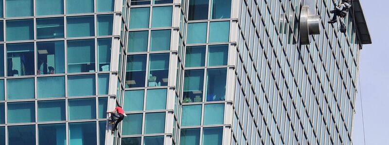 Schaulustige beobachteten Alex Honnold nicht nur vom Boden aus - auch hinter den Bürofenstern wurde der Extremsportler angefeuert. - Foto: ChiangYing-ying/AP/dpa