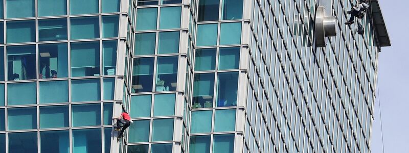 Schaulustige beobachteten Alex Honnold nicht nur vom Boden aus - auch hinter den Bürofenstern wurde der Extremsportler angefeuert. - Foto: ChiangYing-ying/AP/dpa