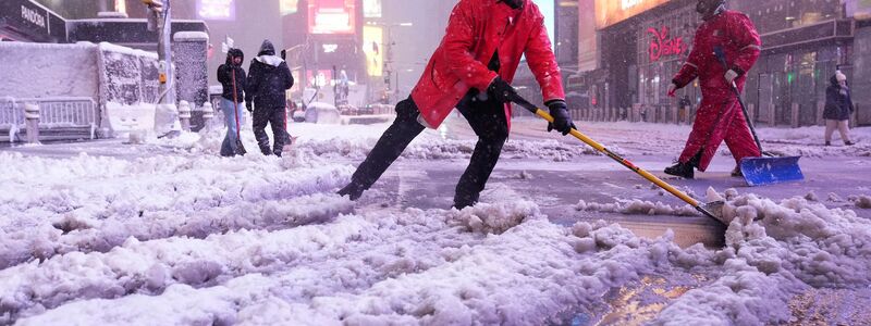 Ein Arbeiter schaufelt Schnee auf dem Times Square in New York. Ein heftiger Schneesturm zieht über den Nordosten der USA hinweg. - Foto: Seth Wenig/AP/dpa