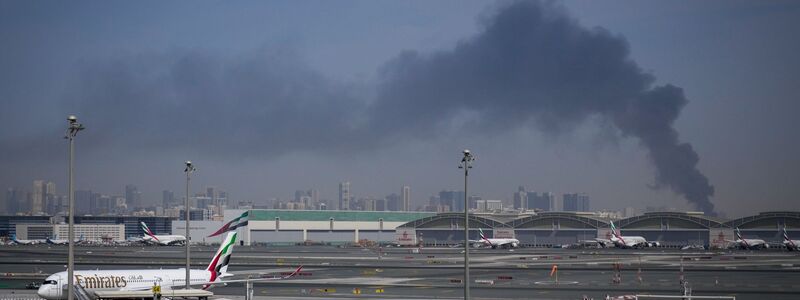 Eine Rauchwolke im Hintergrund, während Flugzeuge auf dem geschlossenen Dubai International Airport geparkt sind. - Foto: Altaf Qadri/AP/dpa